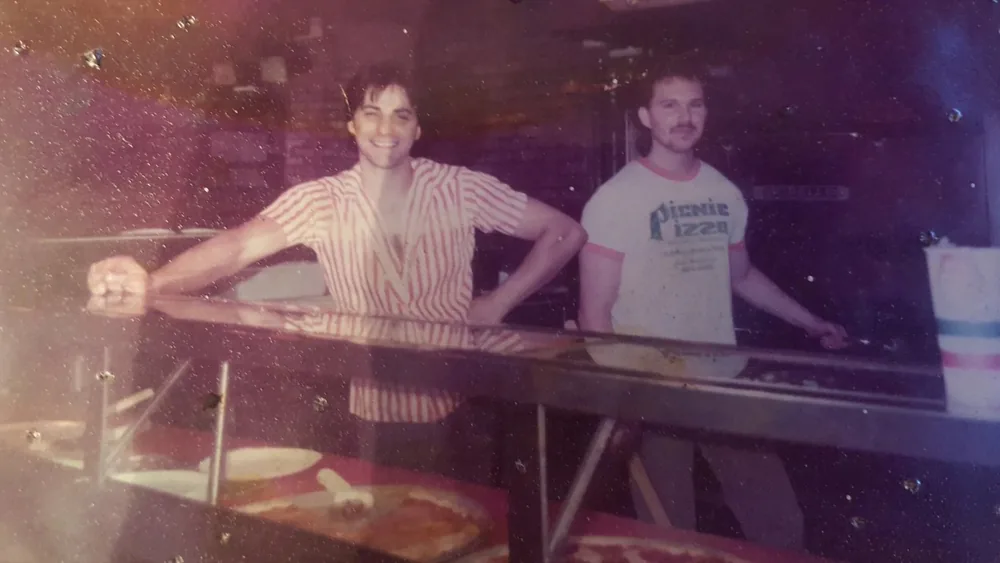 Archive photograph: two men smiling behind the pizza counter, one in a Picnic Pizza t-shirt, pizzas under the glass in front