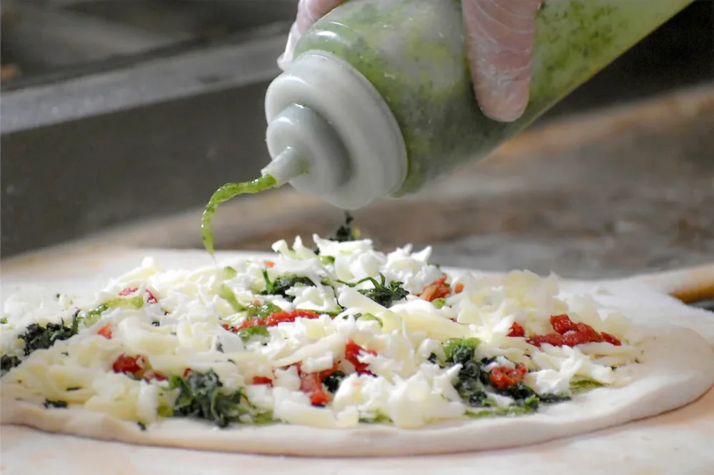 Pesto being added to a pizza