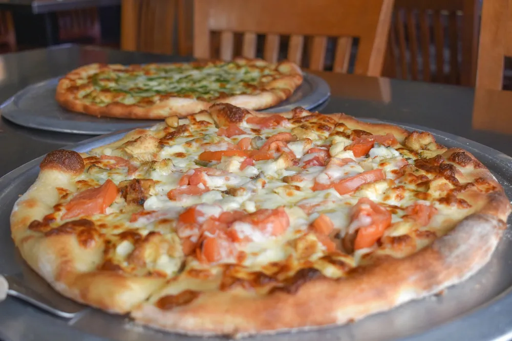 Close view of a fresh-baked pizza with tomato, chicken and browned mozzarella, a pesto pizza behind it
