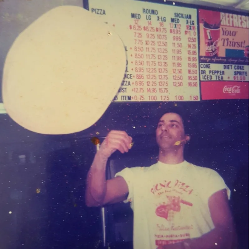 Archive photograph: a pizza maker in a Picnic Pizza t-shirt tossing dough under a hand-lettered menu board